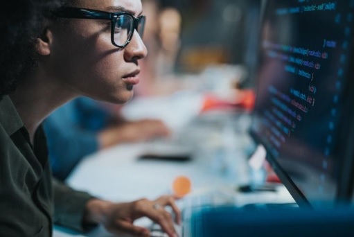 Stock photo of a young woman looking at a computer screen displaying a code editor 