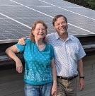 Carol and Andy Phelps standing on the roof of their home with solar panels behind them