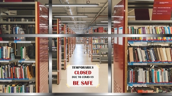 Photo of library stacks with sign reading "Temporarily closed due to COVID-19 Be Safe" in the window